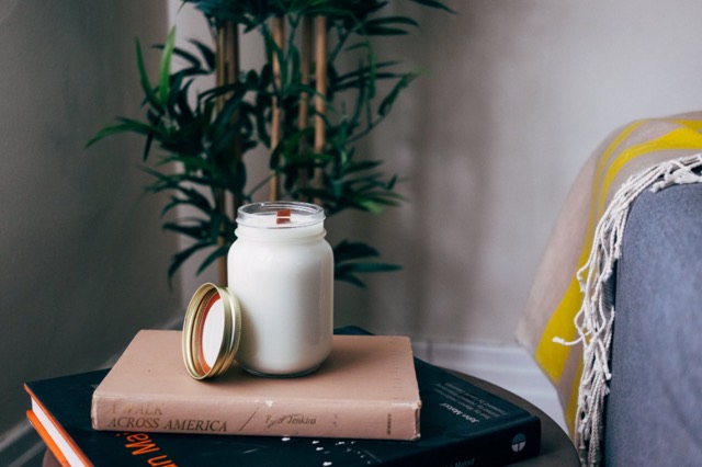 Vela en frasco sobre libros junto a una planta